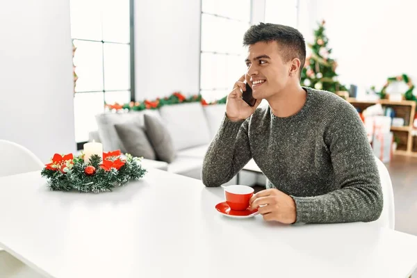 Young Hispanic Man Drinking Coffee Talking Smartphone Sitting Christmas Tree — Stockfoto