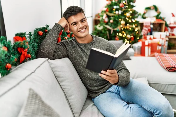 Young Hispanic Man Reading Book Sitting Sofa Christmas Tree Home — 스톡 사진