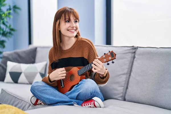 Evdeki koltukta ukelele oynayan genç bir kadın.