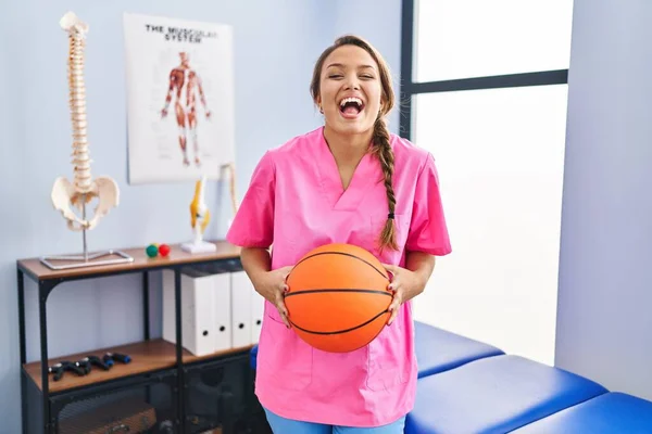 Young Hispanic Woman Working Physiotherapy Clinic Holding Basketball Ball Celebrating — Stock Photo, Image