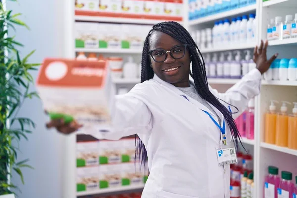 Afro-Amerikalı kadın eczacı gülümseyerek eczanede kendine güvenen bir paket tutuyor.