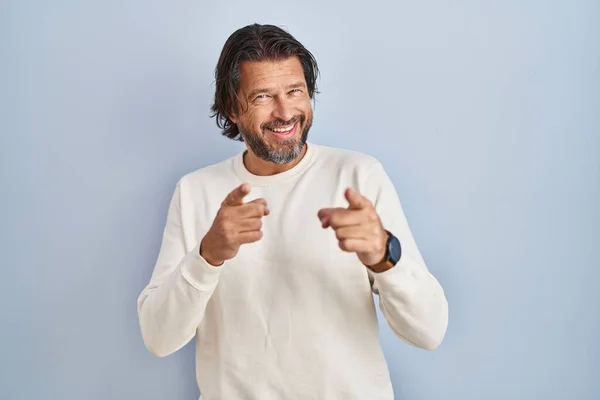 幸せと面白い顔でカメラに指を指して青い背景の上にカジュアルなセーターを着てハンサムな中年の男性 良いエネルギーと振動は — ストック写真