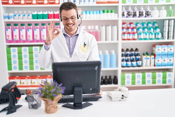 Молодой Латиноамериканец Работающий Аптеке Наушниках Делает Знак Пальцами Улыбаясь Дружелюбный — стоковое фото