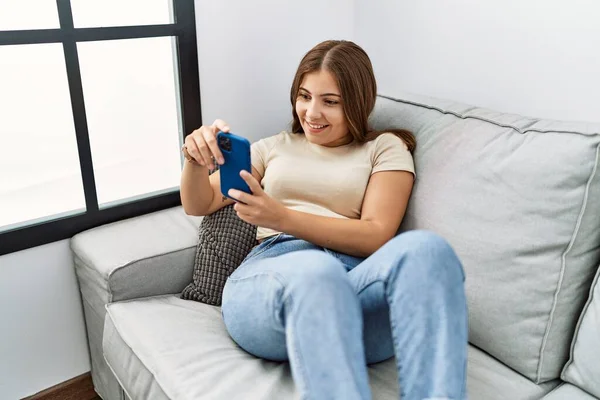 年轻的惊慌失措的女人在家里用智能手机充满自信地微笑 — 图库照片