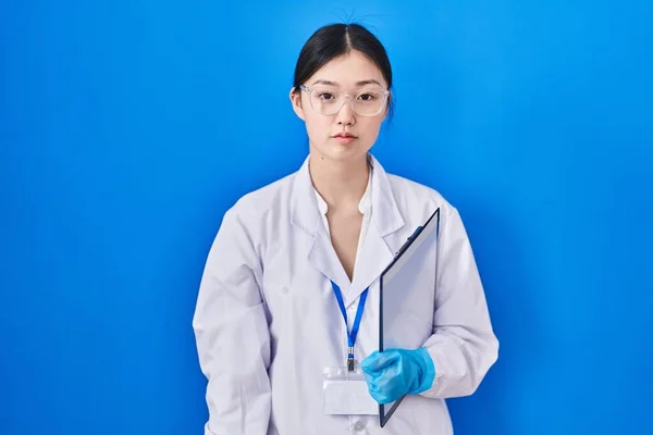 Chinese young woman working at scientist laboratory relaxed with serious expression on face. simple and natural looking at the camera.