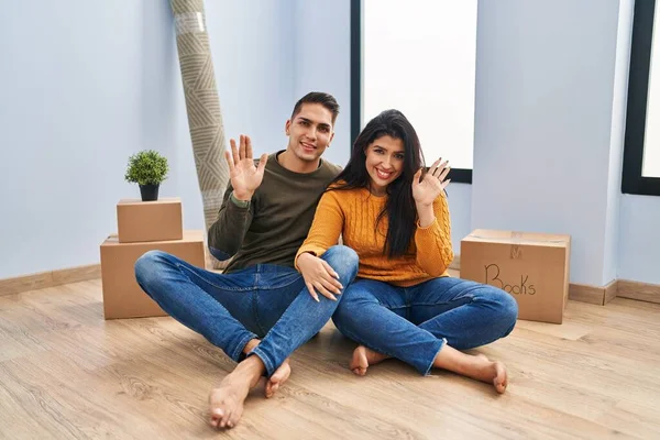 Young Couple Sitting Floor New Home Waiving Saying Hello Happy — Stock Photo, Image