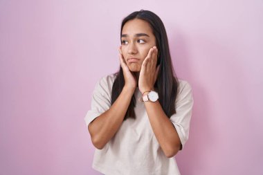 Pembe arka planda duran genç İspanyol kadın. Yorgun eller, yüzü, depresyonu ve üzüntüyü örten, sorun yüzünden üzgün ve tedirgin. 
