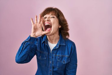 Orta yaşlı bir kadın pembe arka planda durup el pençe divan çığlıklar atıyor. iletişim konsepti. 