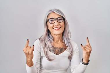 Beyaz arka planda gri saçlı, çılgın bir ifadeyle el kaldırarak rock sembolü yapan orta yaşlı bir kadın. Müzik yıldızı. ağır müzik konsepti. 