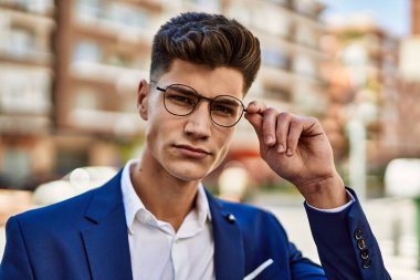 Genç adam sokakta takım elbise ve gözlük takarak rahatladı.