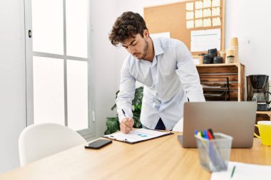 Young hispanic businessman with serious expression working at the office.