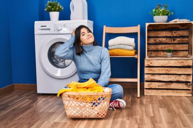 Çamaşır odasındaki genç İspanyol kadın elleri kafasında, şaşırmış ve sinirli yüzüyle stresli ve hayal kırıklığına uğramış 