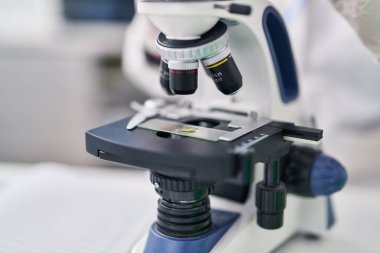 Young hispanic man scientist using microscope working at laboratory