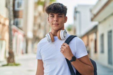 Latin kökenli genç bir öğrenci sokakta kendine güvenen sırt çantası takıyor.