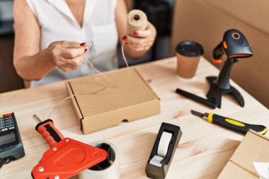 Kıdemli gri saçlı iş kadını ofiste paket siparişi hazırlıyor.