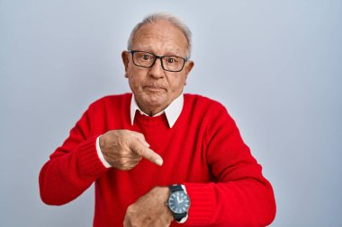 Gri saçlı yaşlı adam tecrit edilmiş arka planda dikiliyor. Aceleyle zamanı, sabırsızlığı ve gecikmeyi gösteriyor. 