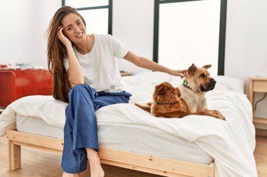 Genç İspanyol kadın gülümsüyor. Yatakta köpeklerle oturuyor.