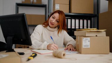 Genç kızıl saçlı kadın ecommerce iş işçisi ofiste kitap yazıyor.