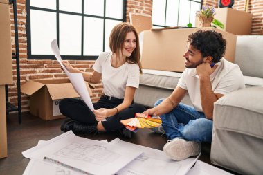 Erkek ve kadın, gülümseyen ve kendine güvenen bir çift yeni evinde boya rengi seçiyor.