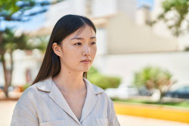 Parkta rahat bir ifadeyle yan tarafa bakan Çinli kadın.