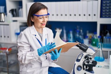 Orta yaşlı bilim kadını, laboratuarda kendinden emin bir şekilde kitap okurken gülümsüyor.