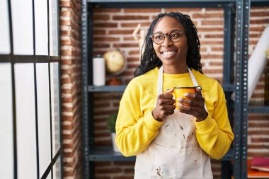 Afro-Amerikan kadın sanatçı gülümsüyor. Sanat stüdyosunda kahve içiyor.