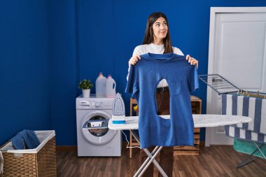 Çamaşır odasında ütü yapan genç esmer kadın. Elinde yanmış demir gömleği vardı. Gülümsüyor ve başka tarafa bakıyordu.. 