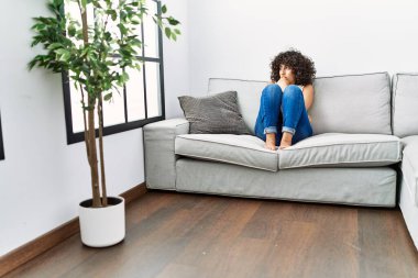 Ortadoğulu genç bir kadın evdeki kanepede oturuyor.