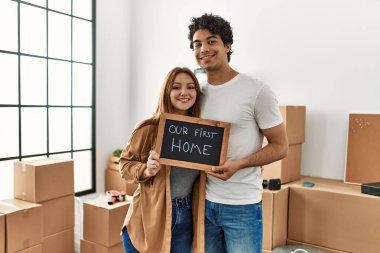 Genç çift yeni evimizdeki ilk mesajımızla birlikte mutlu bir şekilde ellerinde tahtayla gülümsüyor..