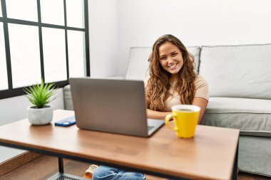 Güzel İspanyol kadın bilgisayarını evde kullanıyor ve kollarını kavuşturup kameraya gülümsüyor. pozitif kişi. 