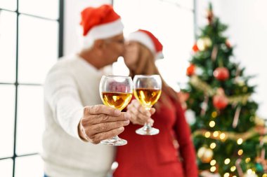 Orta yaşlı İspanyol çift evde Noel ağacının yanında öpüşüp şampanya içiyor..