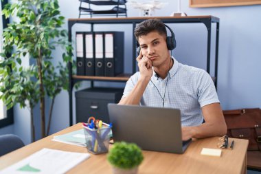 Ofiste çalışan, kulaklık takan genç İspanyol adam kollarını kavuşturup depresyondan sıkılmış ve yorgun göründüğünü düşünüyor.. 