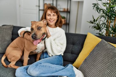 Beyaz bir kadın gülümsüyor. Kendine güvenen bir köpek. Evdeki kanepede oturuyor.