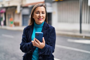 Sokakta akıllı telefon kullanan orta yaşlı bir iş kadını.