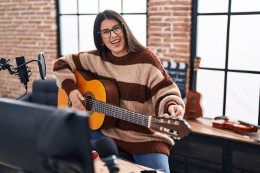 Young hispanic woman musician playing spanish guitar at music studio