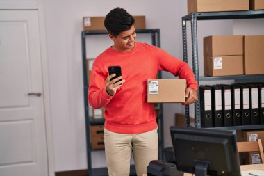 Genç bir İspanyol iş adamı ofiste akıllı telefon paketi kullanıyor.