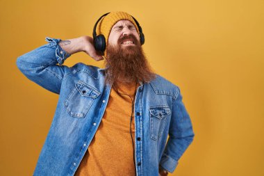 Uzun sakallı beyaz bir adam kulaklık takıp müzik dinliyor. Boyun ağrısı çekiyor. Boynuna elle dokunuyor. 