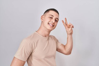 İzole edilmiş arka planda duran genç adam kameraya bakıp zafer işareti yapıyor. İki numara.. 