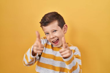 Sarı arka planda duran genç beyaz çocuk mutlu ve komik yüzüyle kamerayı işaret ediyor. iyi enerji ve titreşimler. 