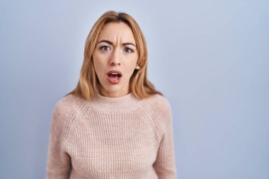 Mavi arka planda duran İspanyol kadın şaşkınlık ve şaşkınlık ifadesi, korku ve heyecan dolu yüz ifadesiyle dehşete düşmüş ve şok olmuştu.. 