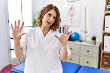 Orta yaşlı fizyoterapist kadın ağrı kesici kliniğinde çalışıyor. Korkudan ve korku ifadesinden korkuyor. El hareketlerini durdur, şok içinde bağır. panik konsepti. 