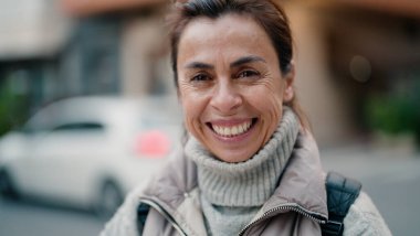 Orta yaşlı İspanyol kadın sokakta kendine güvenerek gülümsüyor.