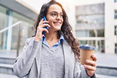 Genç İspanyol kadın yönetici kahve içiyor ve caddede akıllı telefondan konuşuyor.
