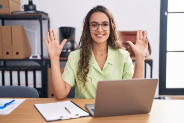 Ofiste çalışan genç İspanyol kadın gözlük takıyor ve dokuz numaralı parmaklarıyla işaret edip gülümserken kendinden emin ve mutlu.. 