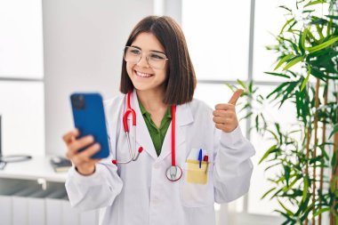 Latin asıllı genç doktor mutlu ve pozitif gülümseyen, mükemmel ve onaylı bir işaret veren bir randevu üzerinde çalışıyor. 