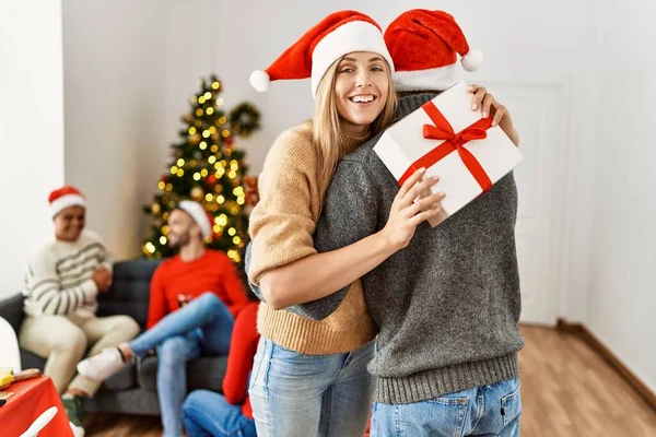 クリスマス会に若い人たちのグループ 夫婦は贈り物を保持し 家で抱擁 — ストック写真
