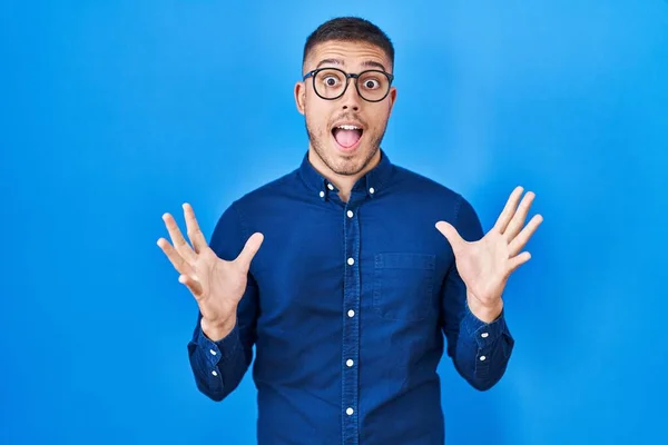 Jovem Hispânico Vestindo Óculos Sobre Fundo Azul Celebrando Louco Espantado — Fotografia de Stock