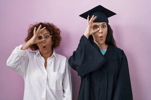 ヒスパニックな母親と娘の卒業キャップと式のローブを着て驚きの顔でショックを受けたOkジェスチャーを行うと 目の指を見て 信じられない表現 — ストック写真