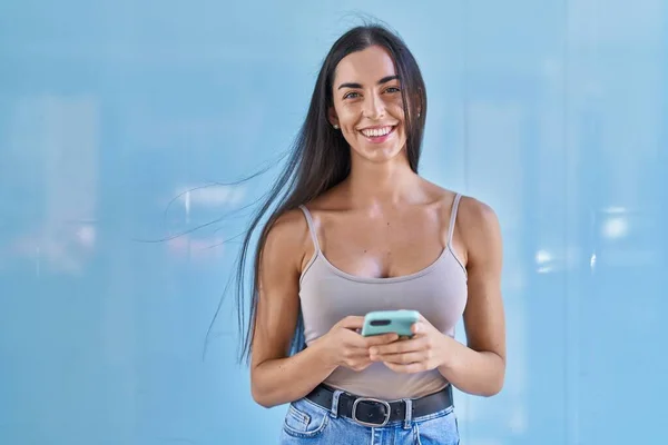 若い美しいですヒスパニック女性笑顔自信を持ってスマートフォンを使用して隔離された青の背景 — ストック写真
