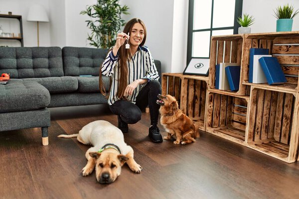 Young hispanic woman holding key of new house sitting on floor with dogs at home